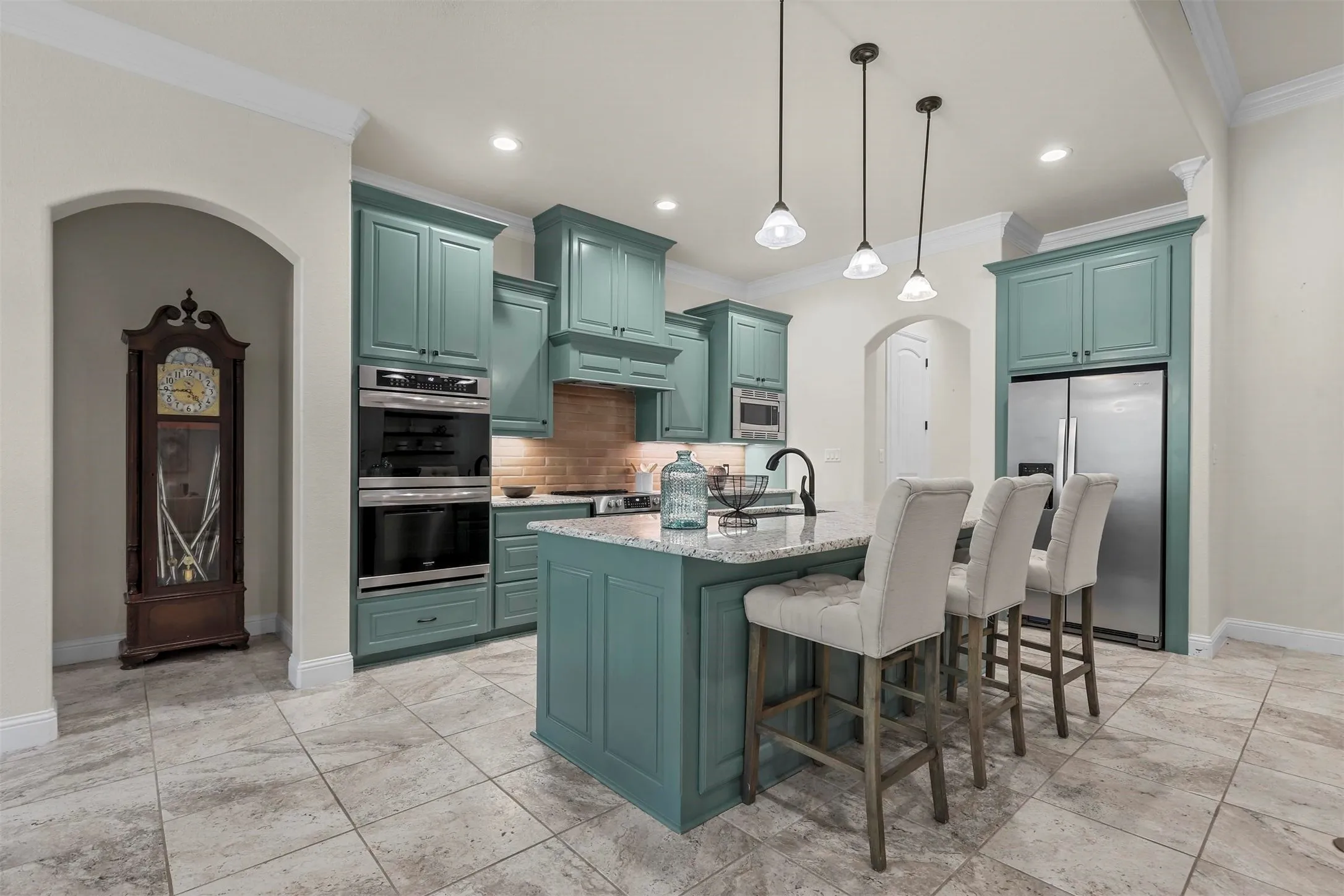 Kitchen featuring a center island with pendant lighting, integrated stainless steel appliances, abundant cabinetry, and tile flooring