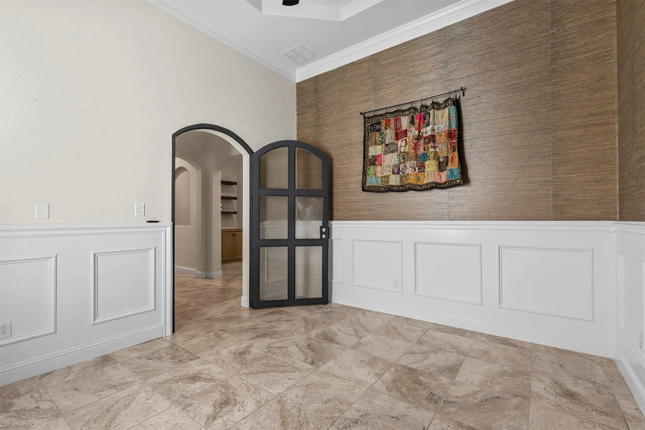Archway entry with a decorative half-door, textured wall accent, and wainscoting