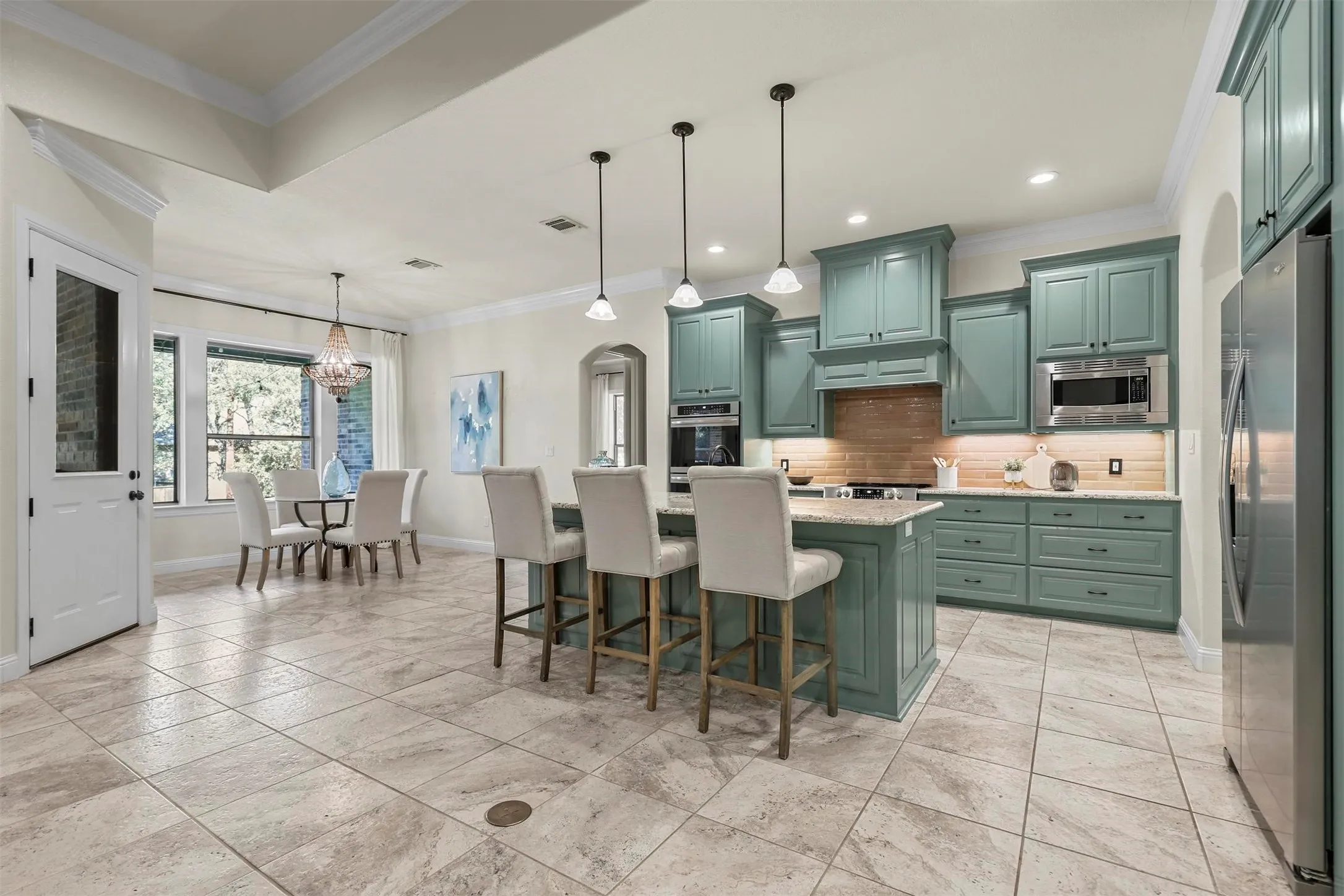 Kitchen featuring light green cabinetry, stainless steel appliances, a center island with pendant lighting, and tile flooring