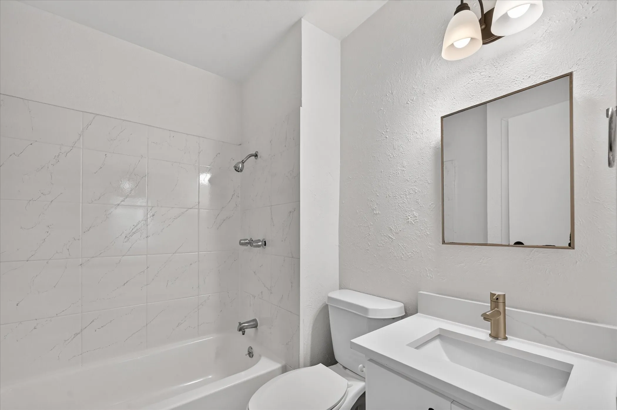 White subway tile shower surround, integrated sink vanity with a single handle faucet, and modern vanity lighting
