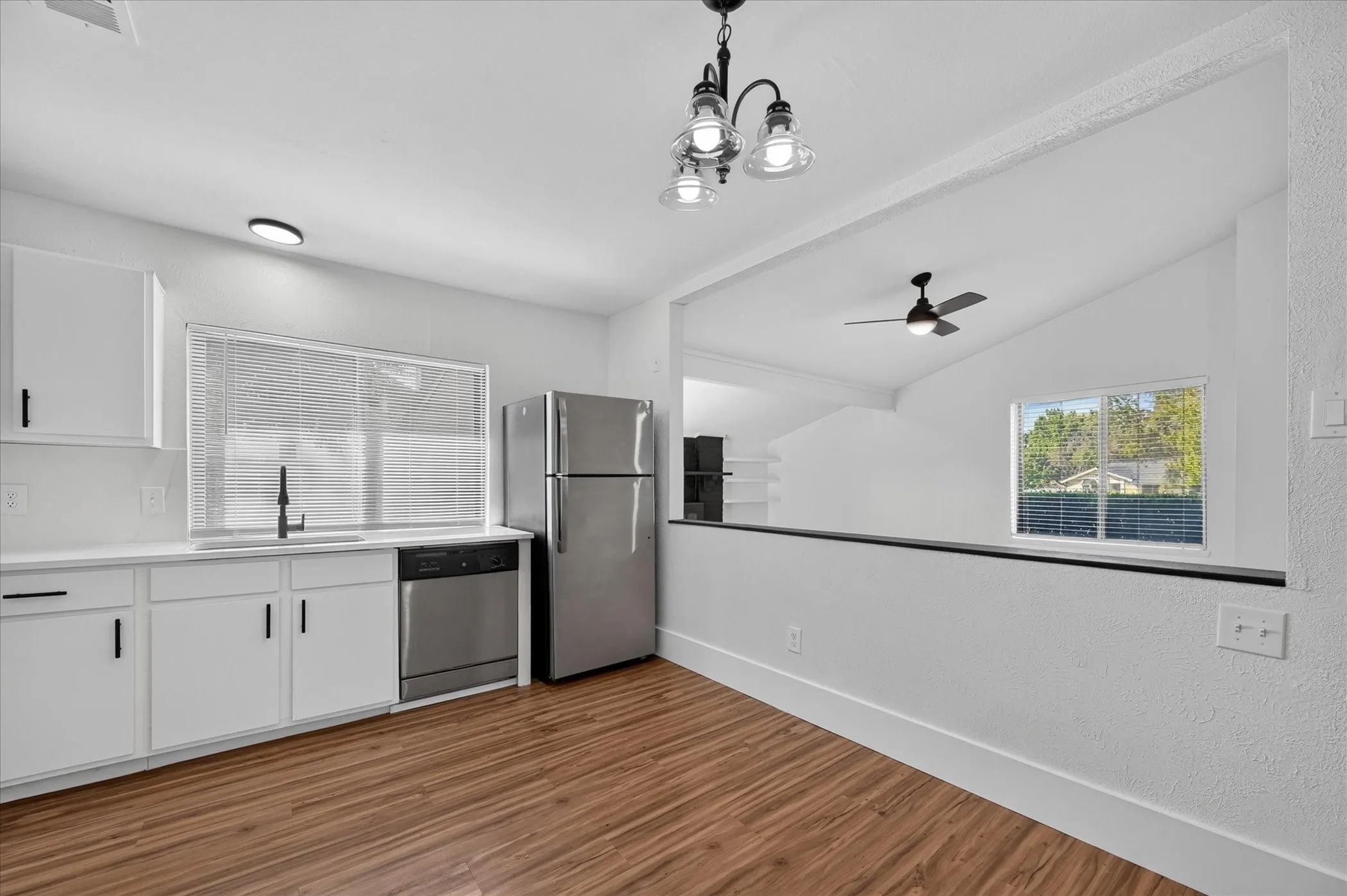 Kitchen featuring white cabinetry, stainless steel appliances, wood-finish flooring, and a contemporary chandelier