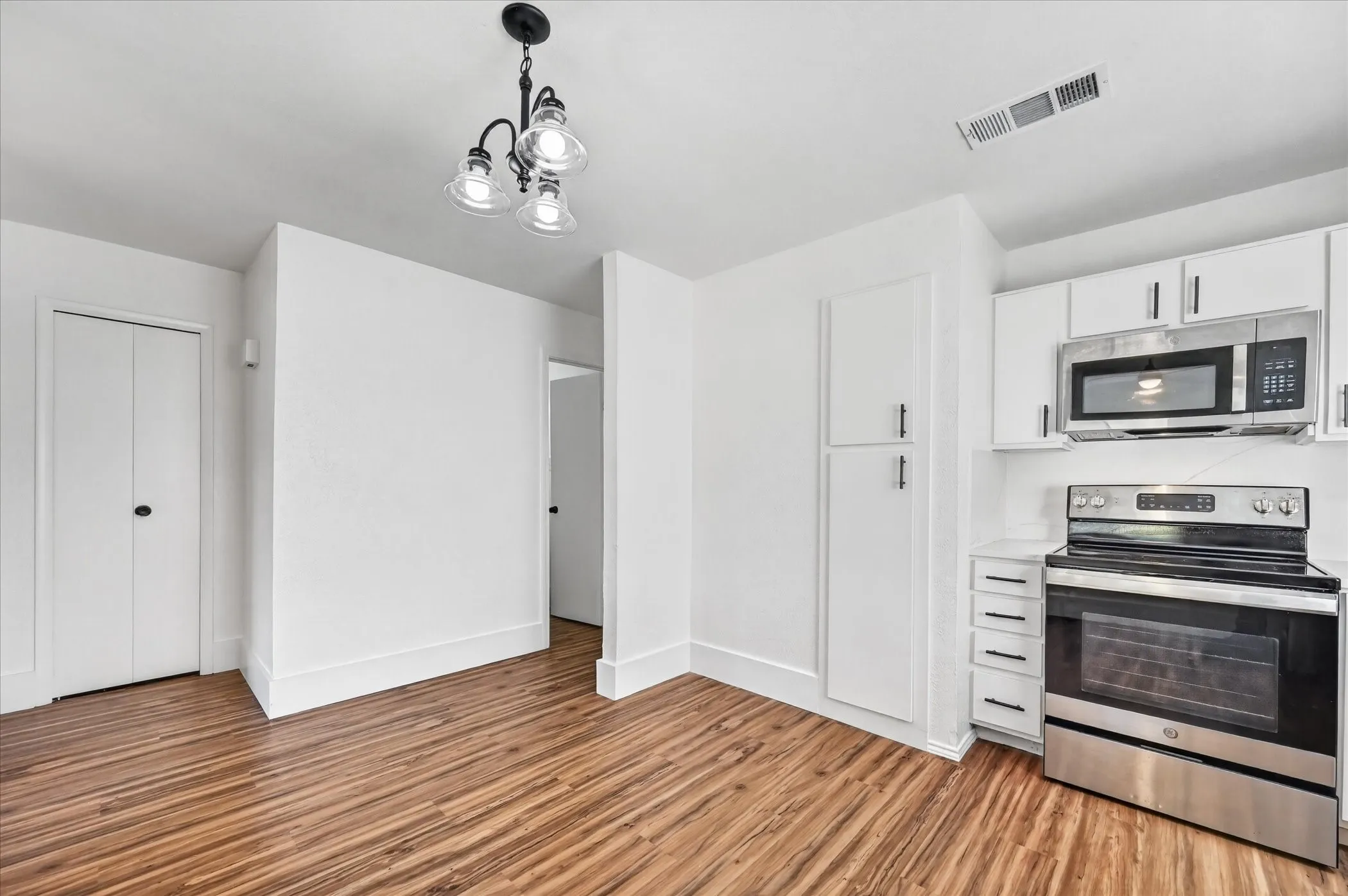 Wood-finish flooring, white cabinetry, stainless steel appliances, and a three-light chandelier
