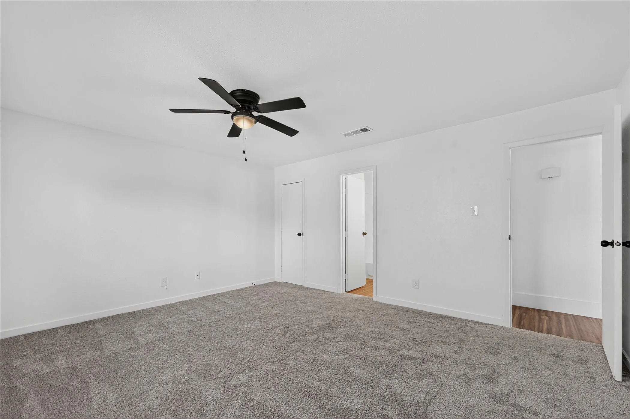 Spacious room featuring neutral carpeting, white walls, a ceiling fan with light, and two doorways