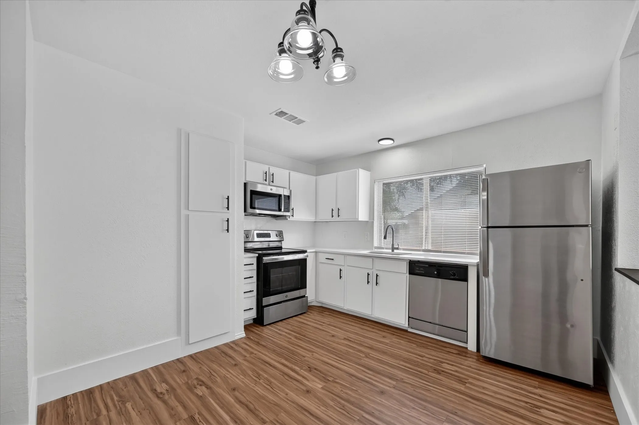 Kitchen featuring wood-finish flooring, white cabinetry, stainless steel appliances, and a built-in microwave