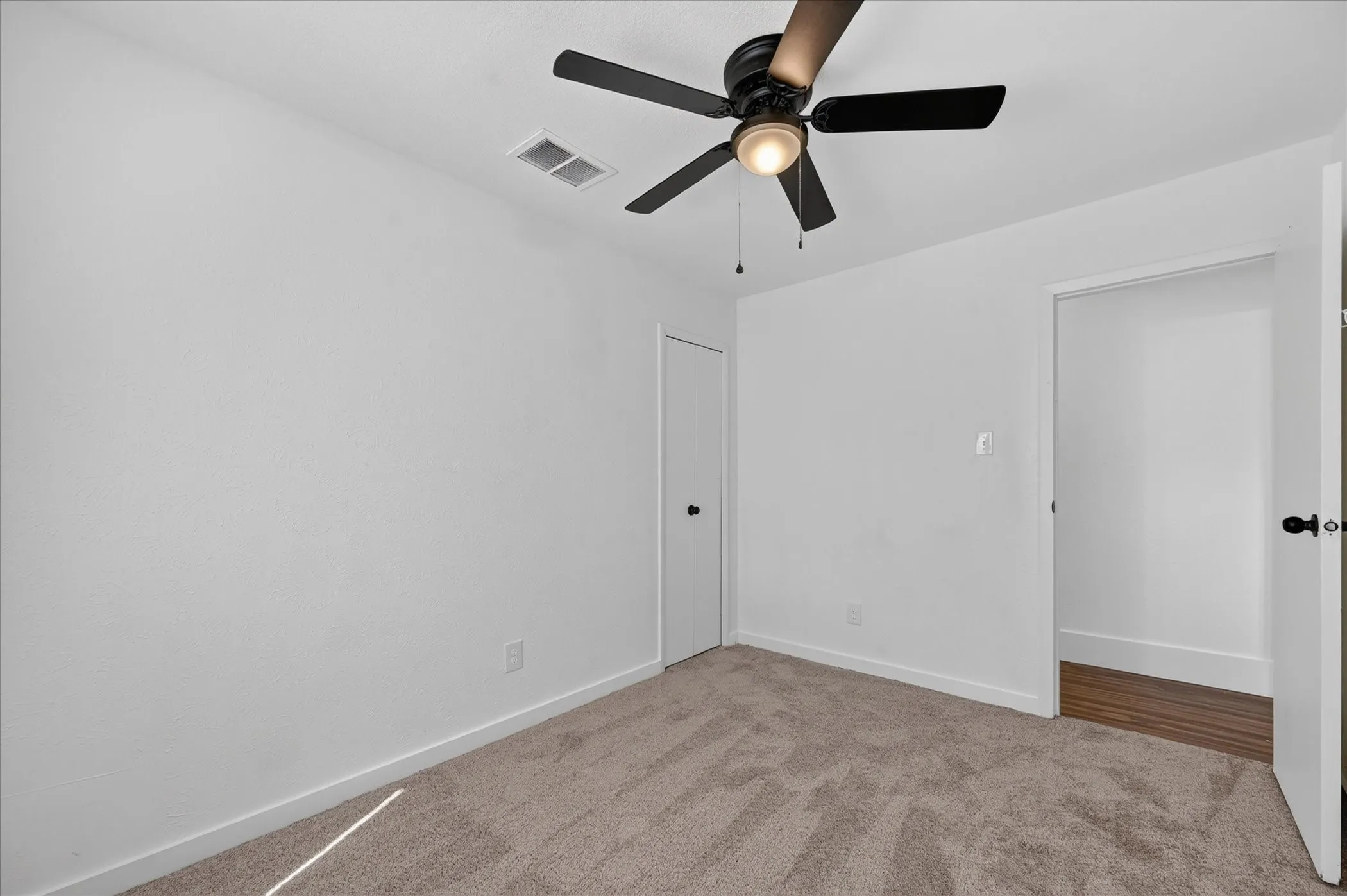 Neutral-toned carpeted flooring, white walls, black ceiling fan with integrated lighting, and white doors with black hardware