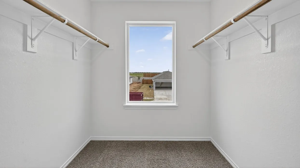 Walk-in closet with window, featuring dual hanging rods, white trim, and neutral carpeting