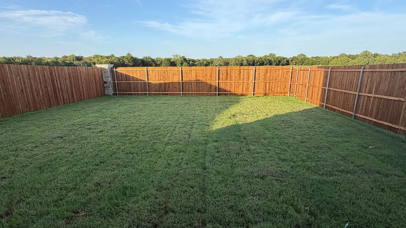 Expansive fenced yard with natural wood-tone privacy fencing and a stone pillar accent