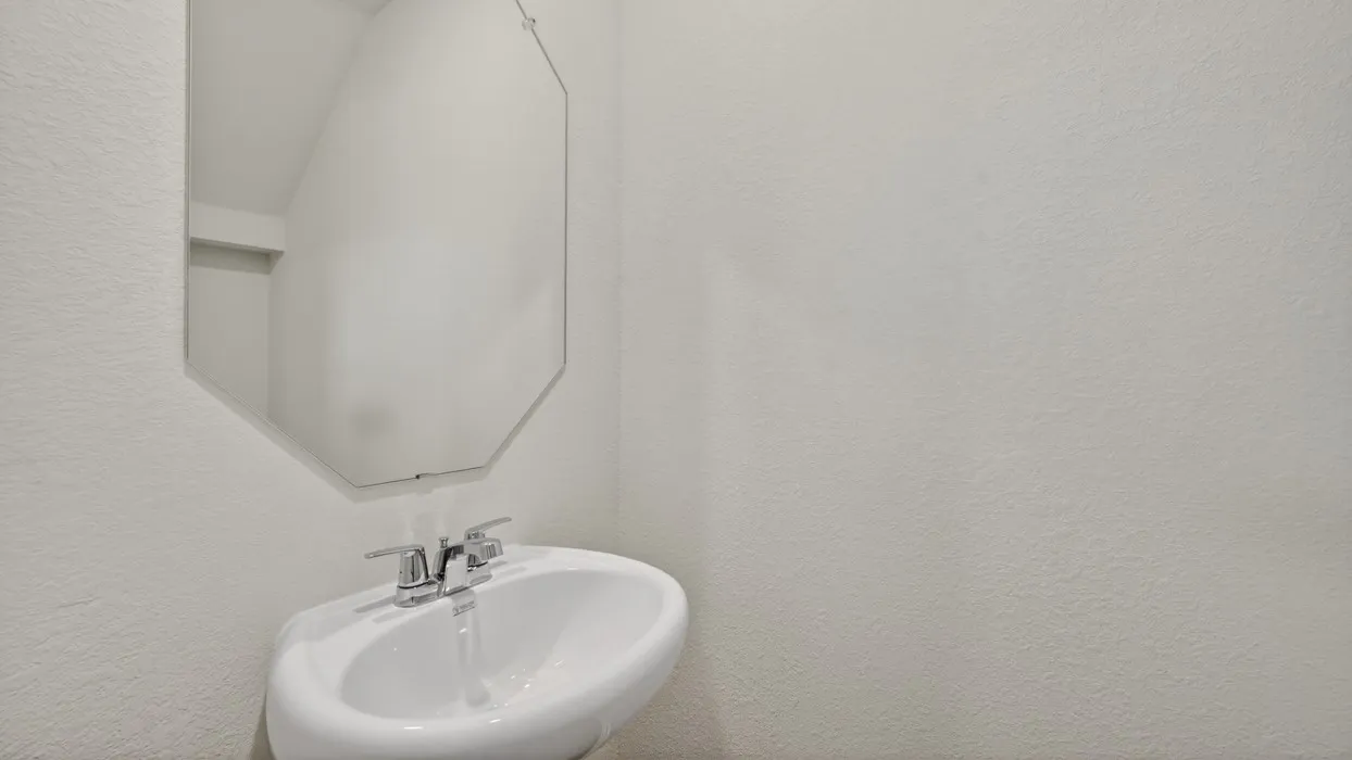 Pedestal sink with chrome fixtures and an octagonal wall mirror
