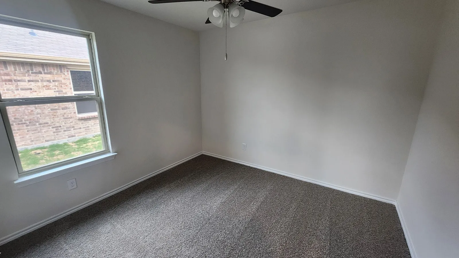 Neutral-toned walls with textured carpeting, a window with white trim, and a ceiling fan with integrated lighting