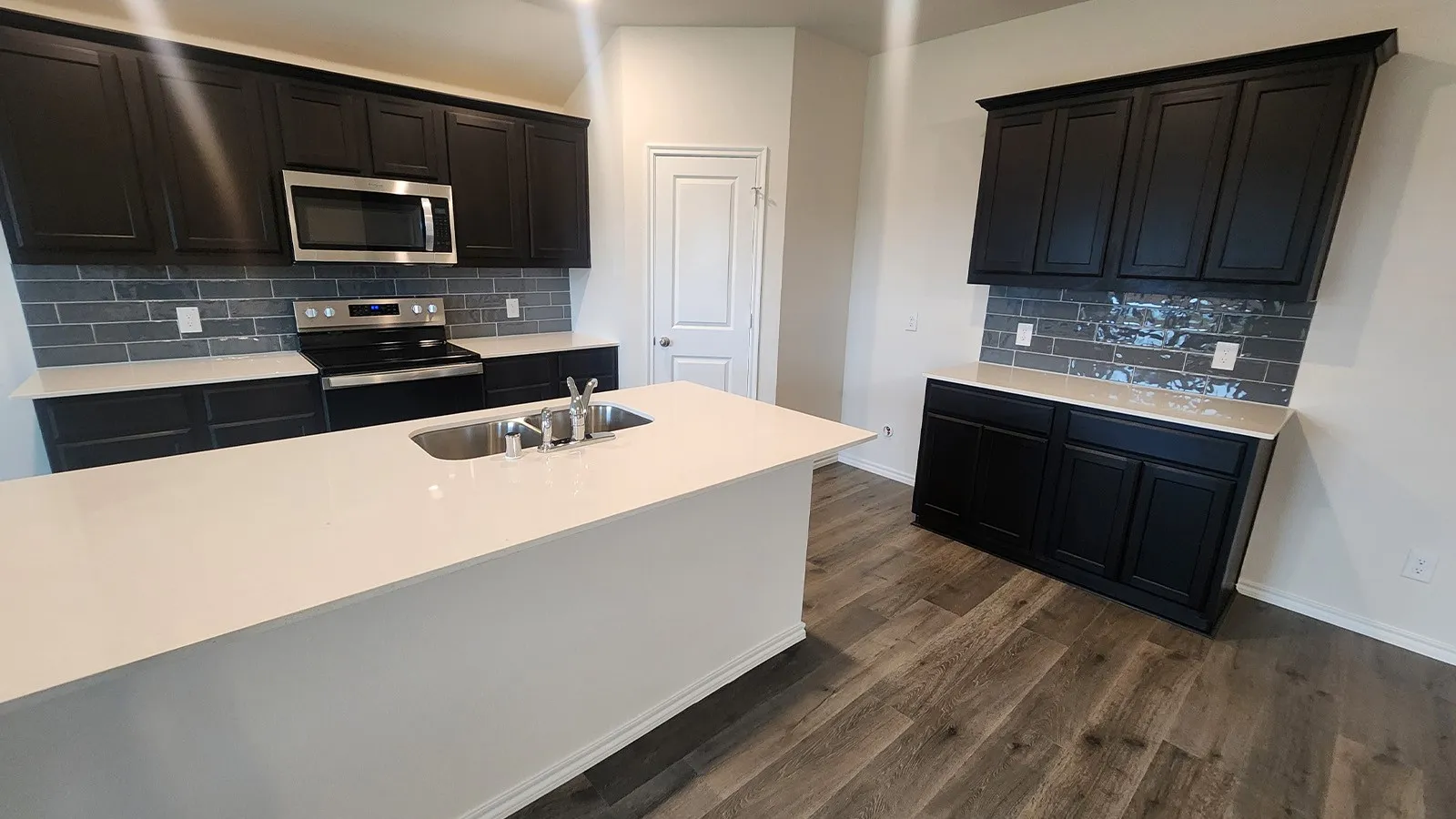 Kitchen featuring dark wood-finish cabinetry, light countertops, subway tile backsplash, stainless steel appliances, and wood-finish flooring