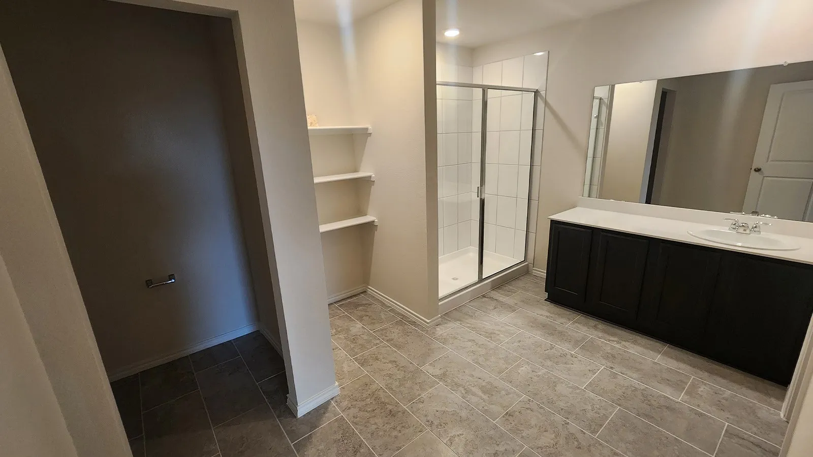 Tile flooring, walk-in shower with glass enclosure, single vanity with dark cabinetry, integrated sink, and large wall-mounted mirror