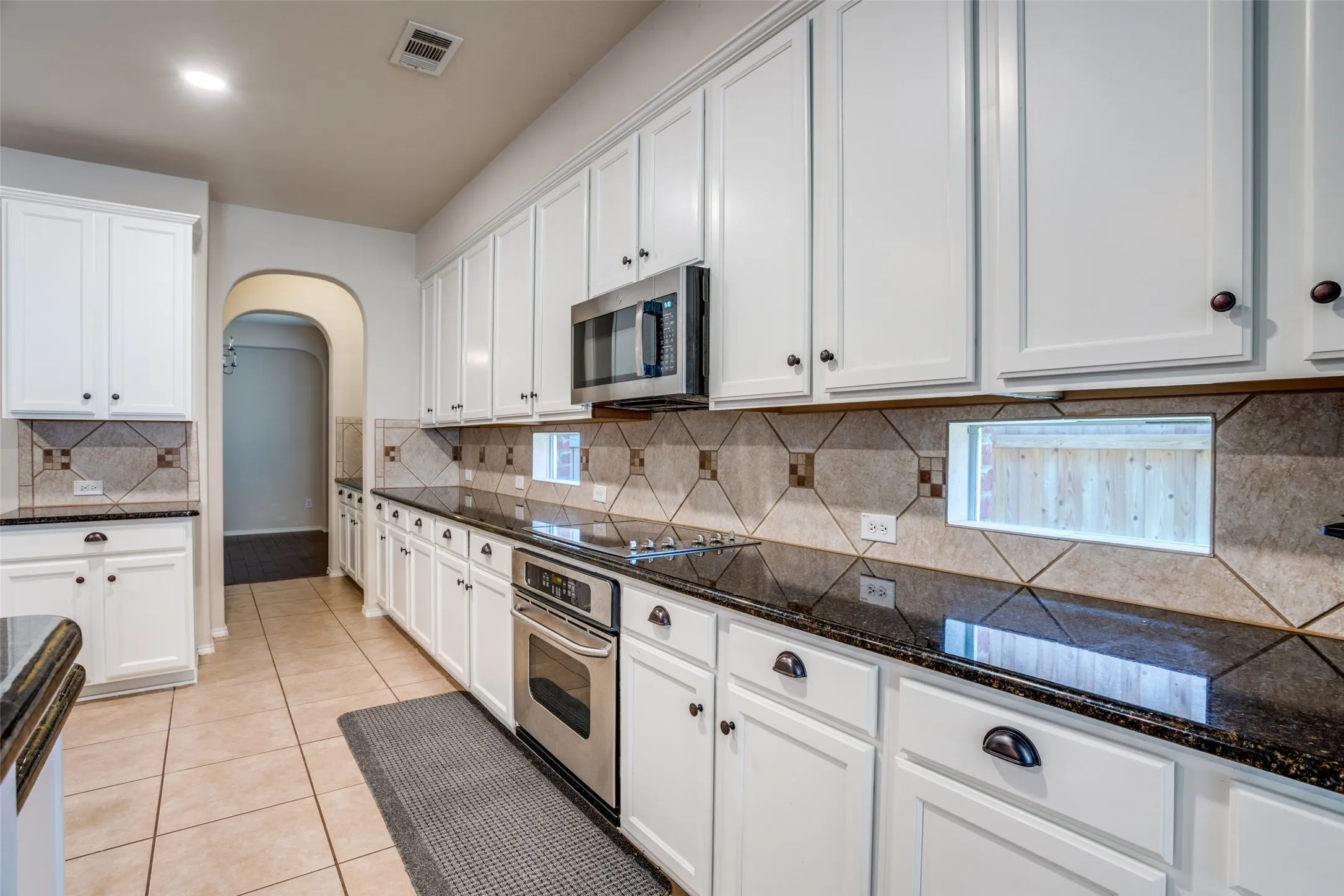 Kitchen with arched walkways, white cabinetry, stainless steel appliances, light tile patterned floors, and dark stone countertops