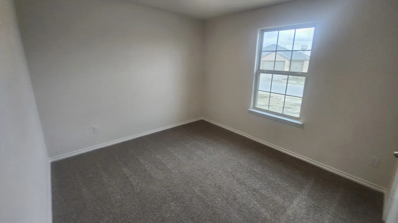 Neutral-toned room featuring a single window with grid panes, textured wall finishes, and a gray carpeted floor