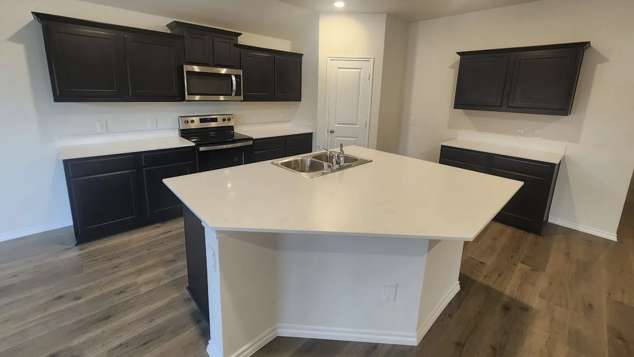 Kitchen featuring a large central island with a double basin sink, white countertops, dark wood-finish cabinetry, stainless steel microwave, and wood-finish flooring