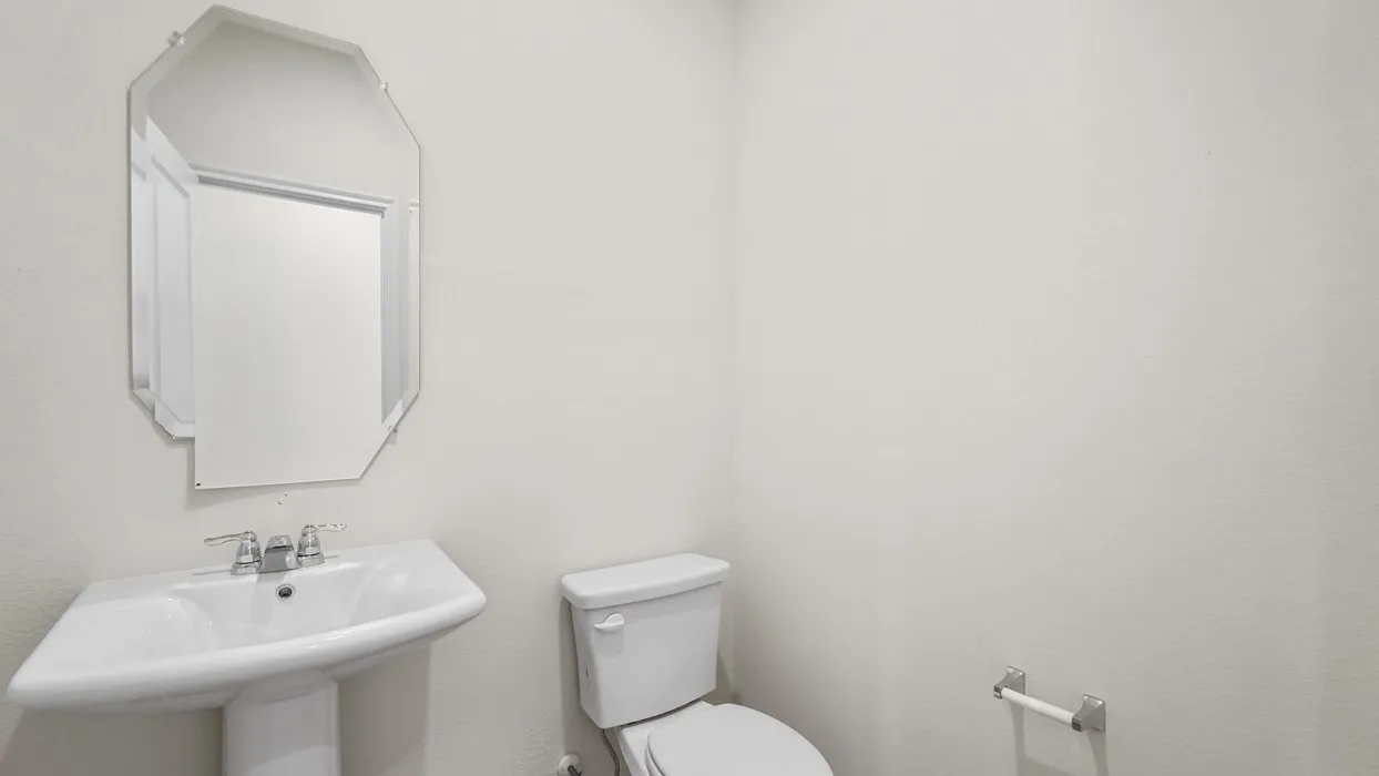 White pedestal sink with chrome faucet hardware, octagonal frameless mirror, and a ceramic toilet