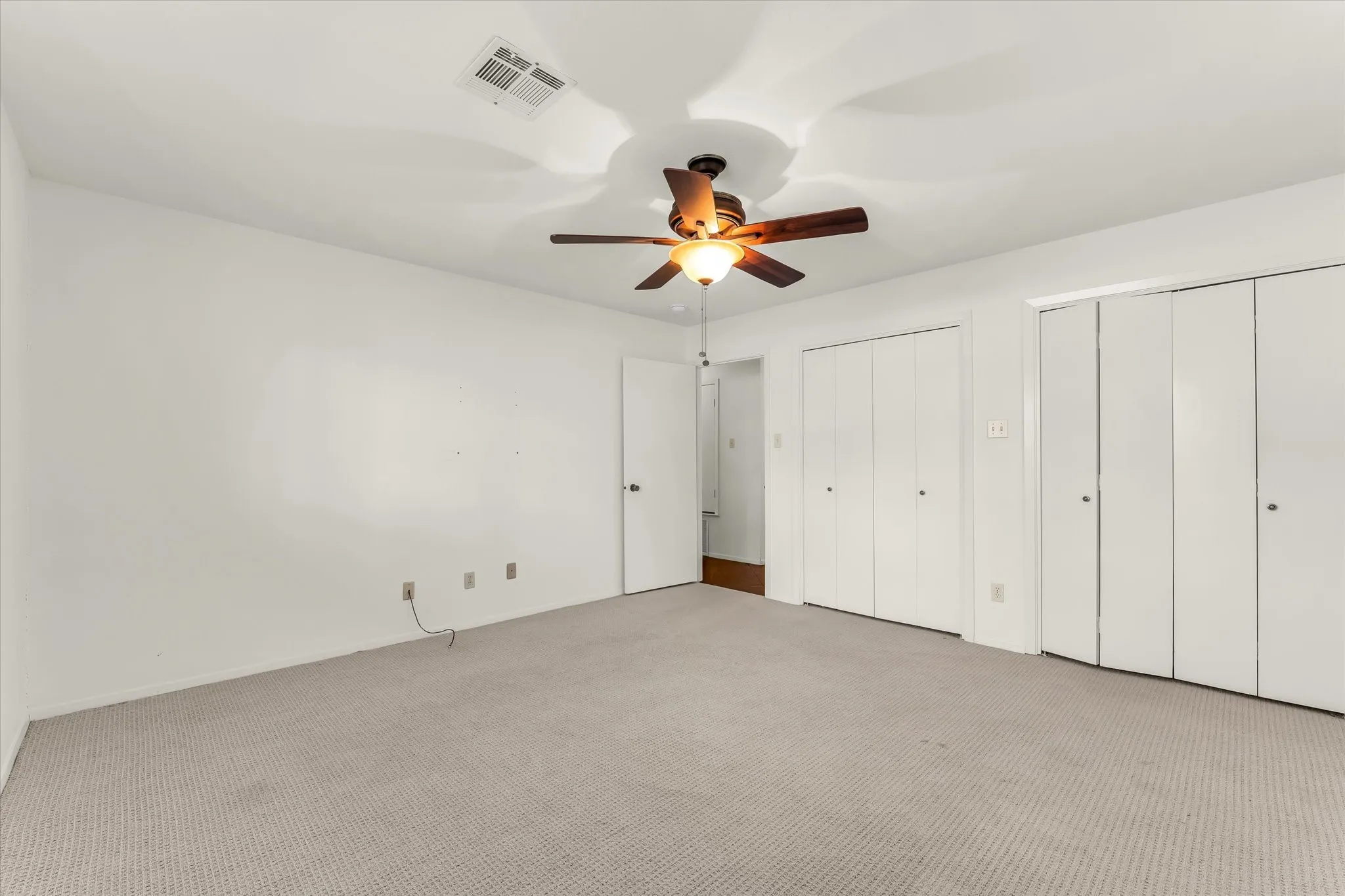 Neutral-toned carpeting, ceiling fan with integrated lighting, multiple bi-fold closet doors, and white painted walls