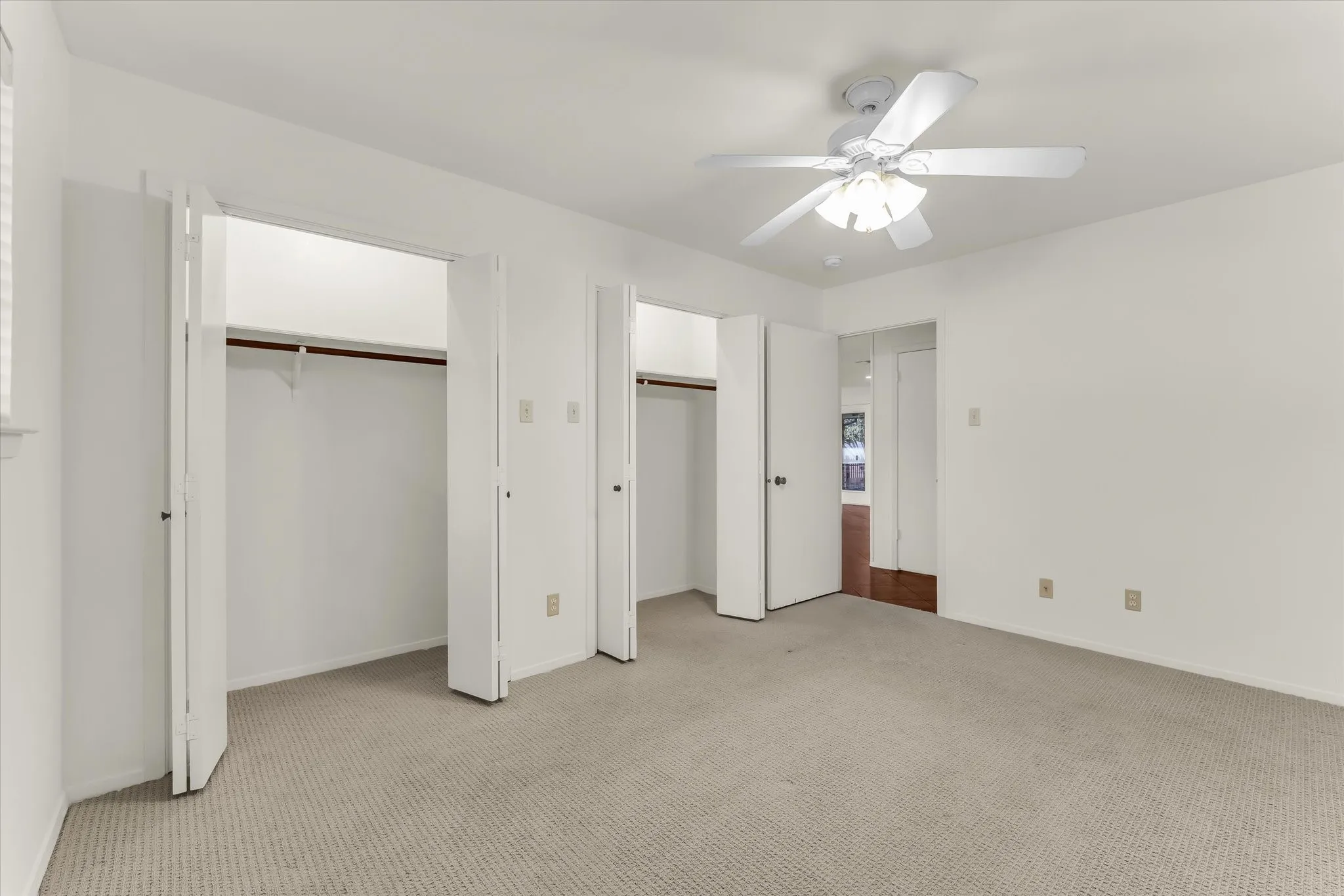 Neutral-toned carpeting, white walls, two bi-fold door closets, and a ceiling fan with integrated lighting