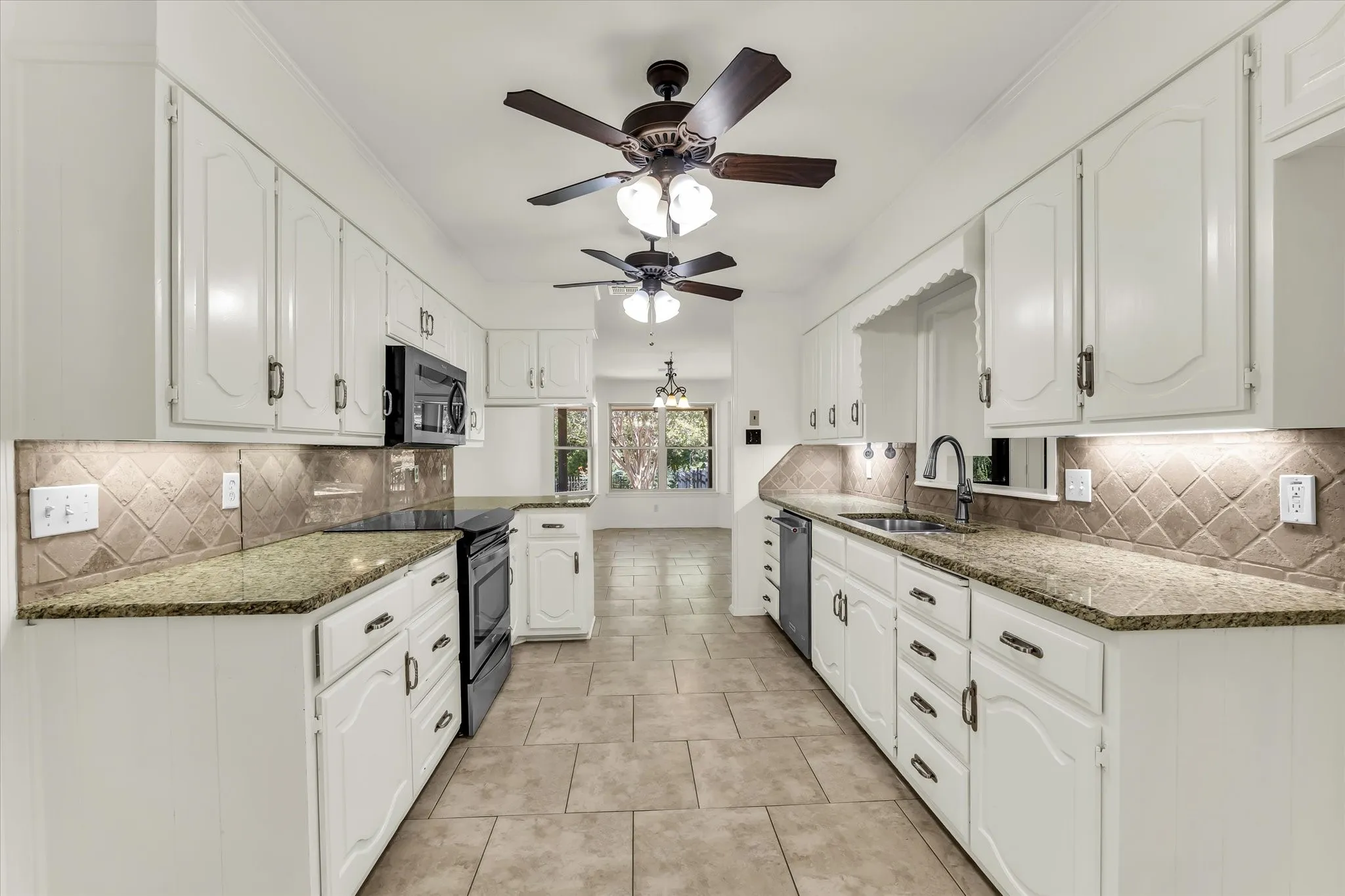Galley kitchen featuring white cabinetry, stone countertops, integrated appliances, ceramic tile flooring, and ceiling fans