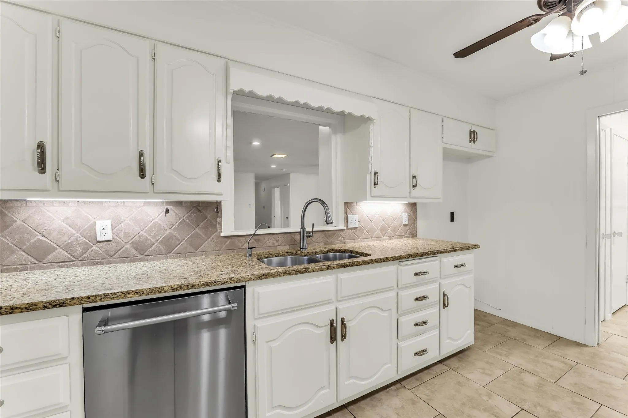 White cabinetry with decorative arch panels, granite countertops, stainless steel dishwasher, tile backsplash, and ceramic tile flooring