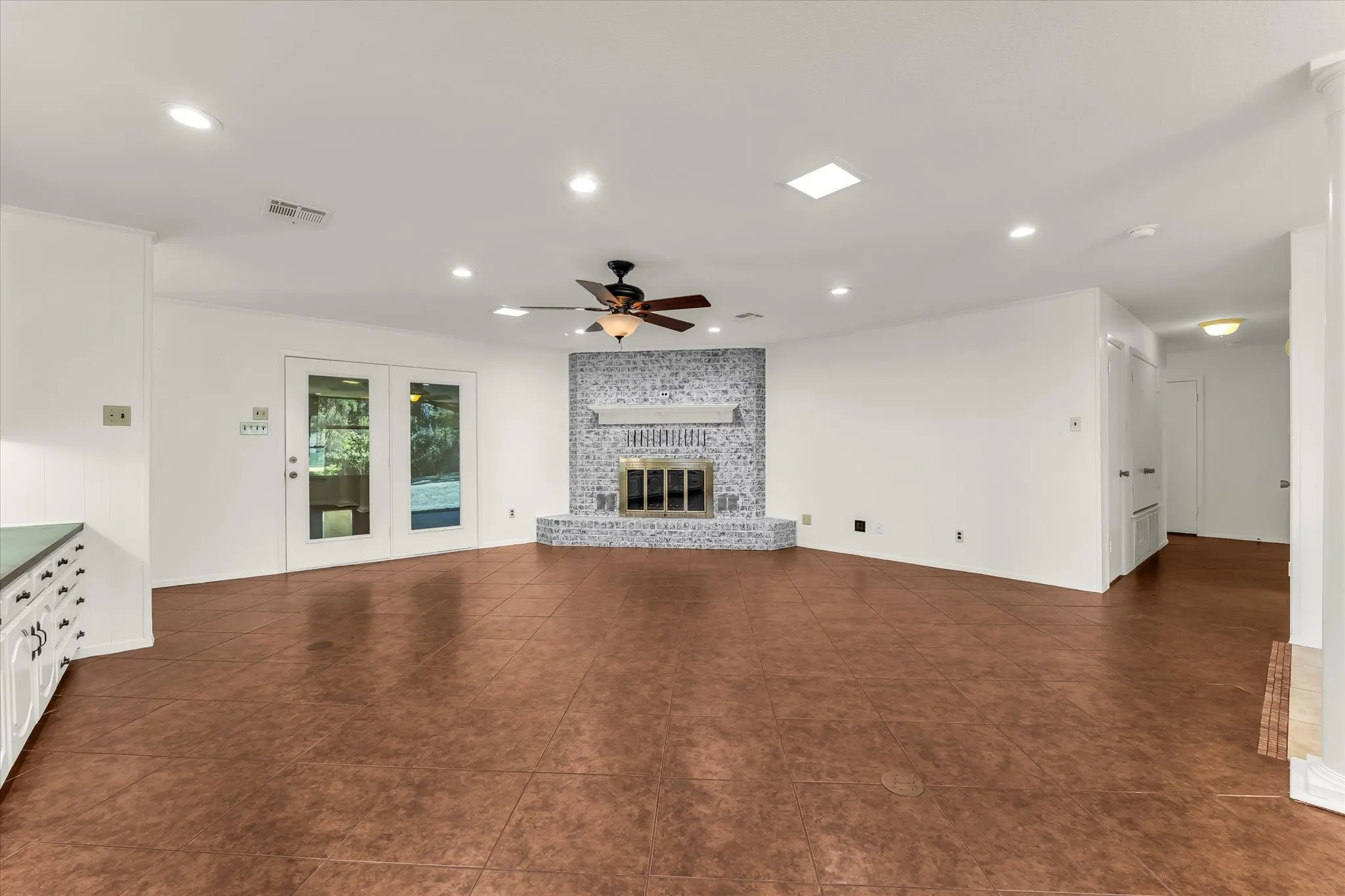 Expansive room featuring wood-finish flooring, a tiled fireplace with mantel, recessed lighting, and a ceiling fan