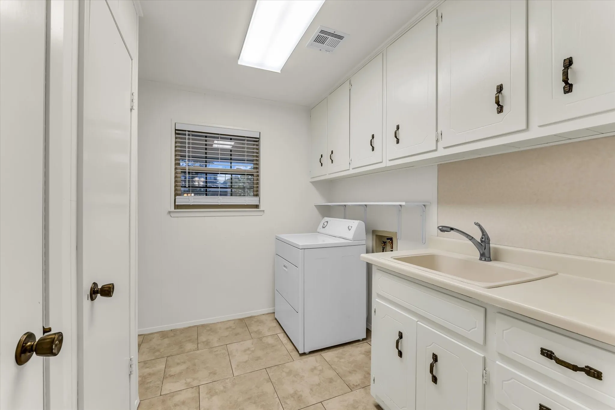 Laundry room featuring extensive white cabinetry, a utility sink with a chrome faucet, and tiled flooring