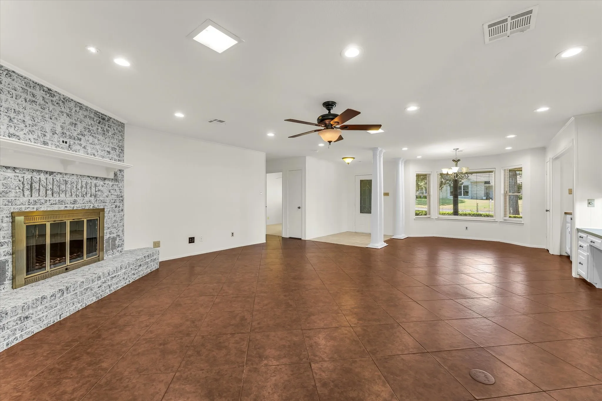Spacious interior with large format tile flooring, a brick fireplace with a mantel, and a ceiling fan