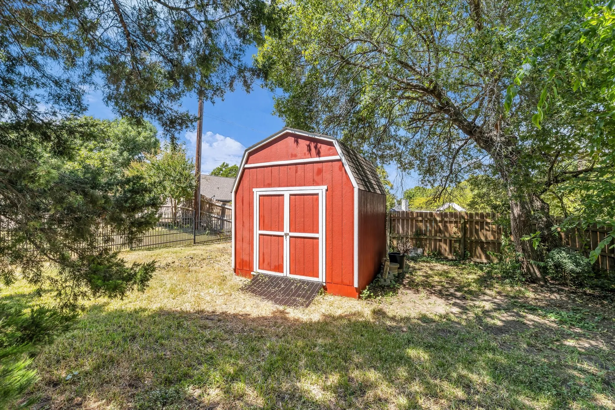 Red barn-style shed with white trim and a shingled roof, set on a grassy area