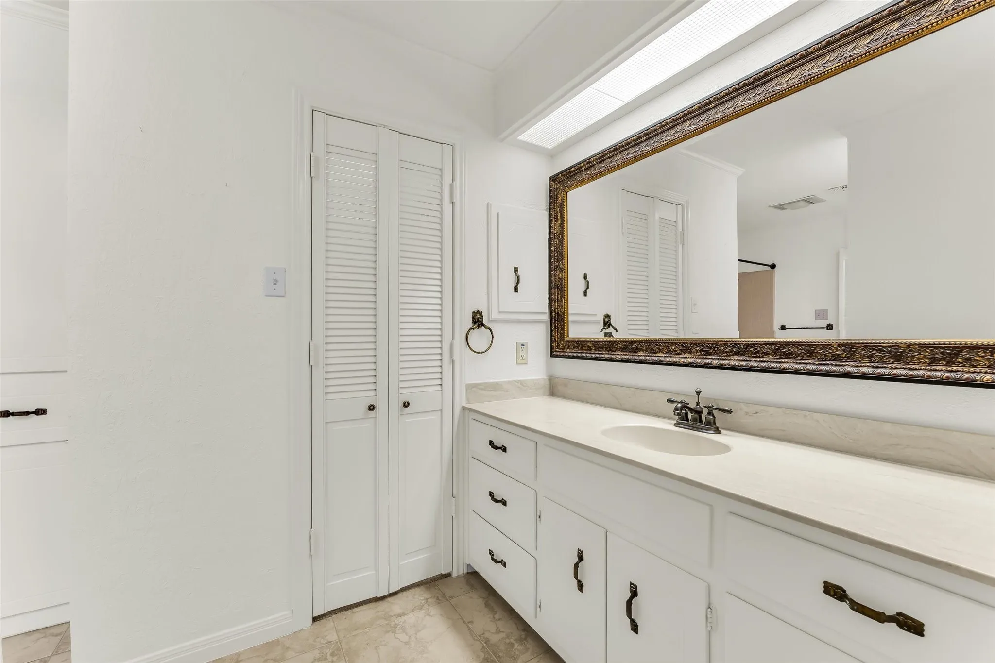 Vanity with an integrated sink, polished chrome faucet, and a large ornate framed mirror