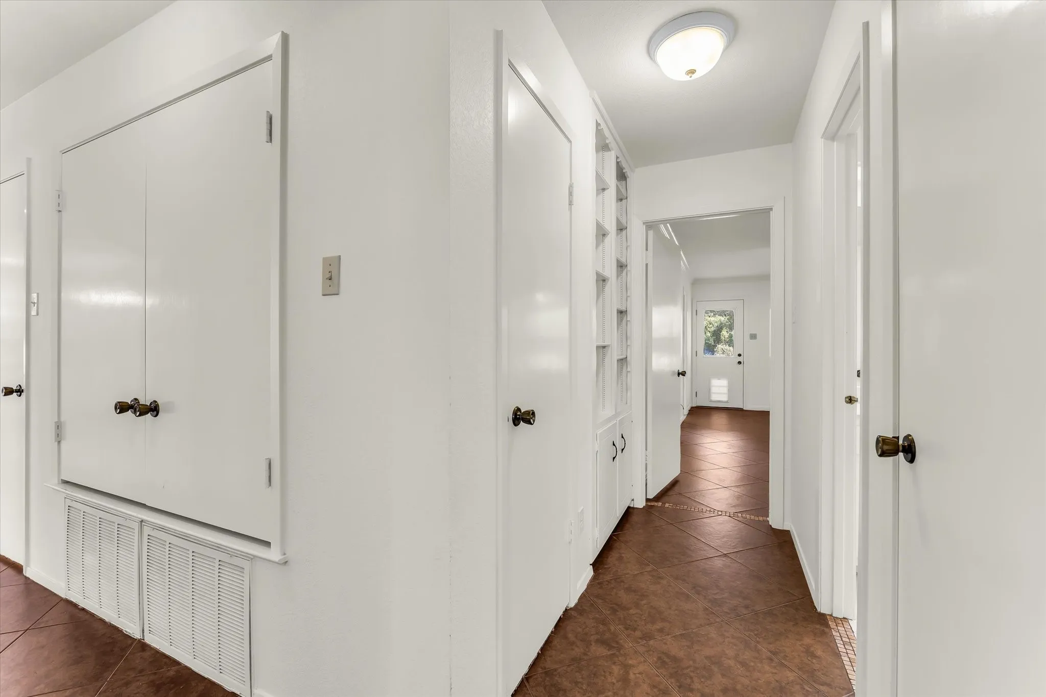 Hallway featuring multiple closet storage with white painted doors and hardware, warm wood-finish flooring, and recessed ceiling lighting throughout