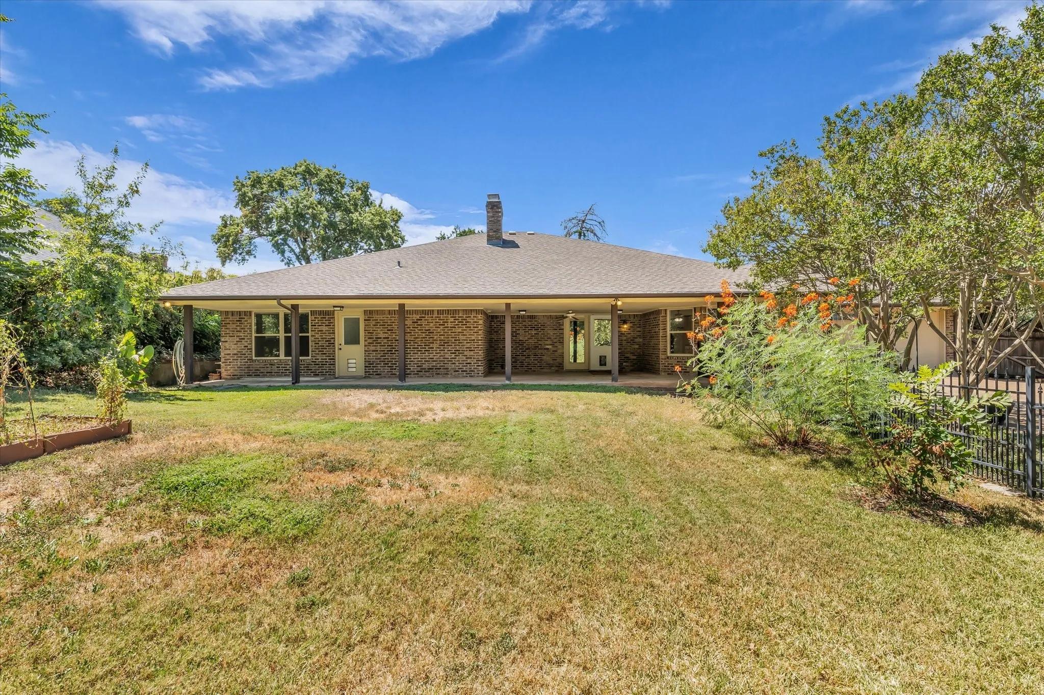 Expansive backyard featuring a brick exterior, covered patio, and mature trees