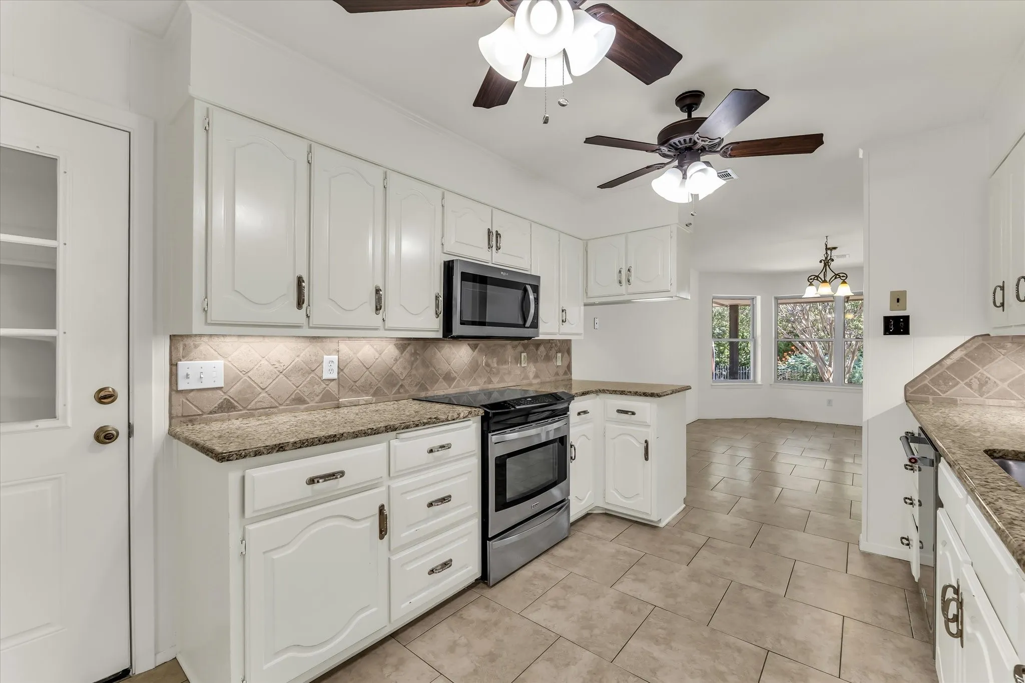 White cabinetry with decorative fronts, stainless steel appliances, granite countertops, tile backsplash, and ceramic tile flooring