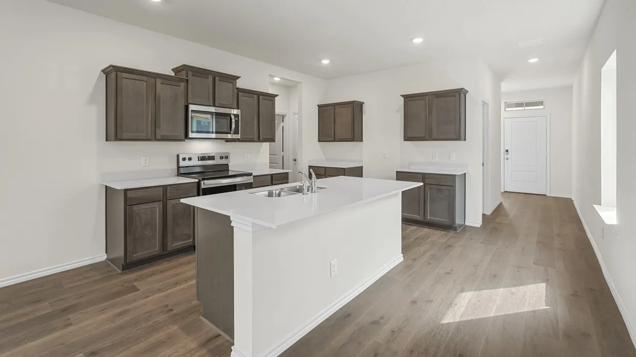 Kitchen featuring an island with a double basin sink, stainless steel appliances, dark wood-finish cabinetry, and light countertops
