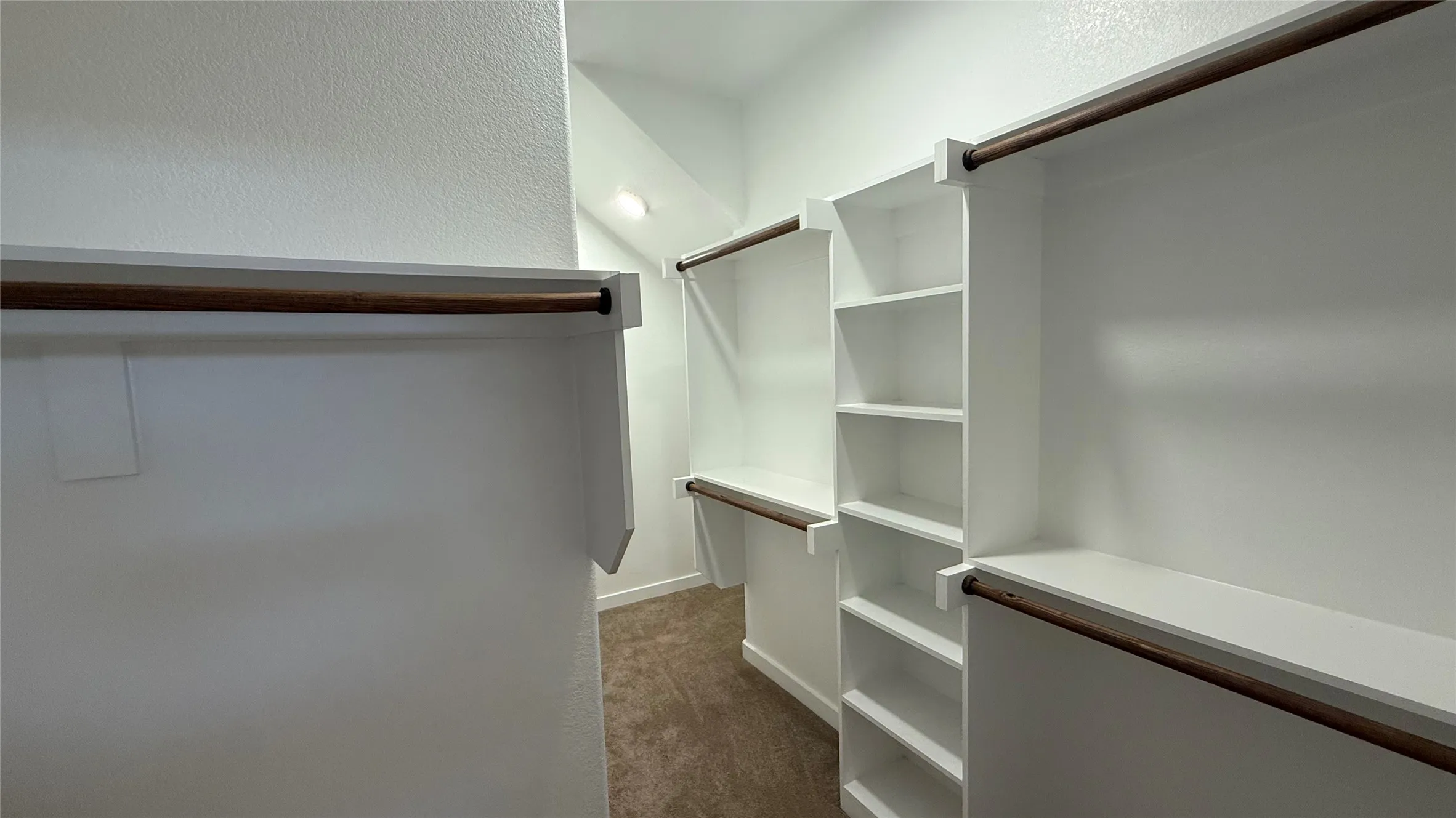 Built-in closet organization with wood-finish rods, shelving, and carpeted flooring