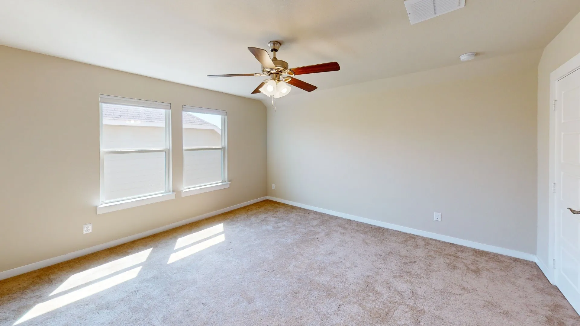 Plush carpeting, neutral wall tones, two large windows, and a ceiling fan with integrated lighting