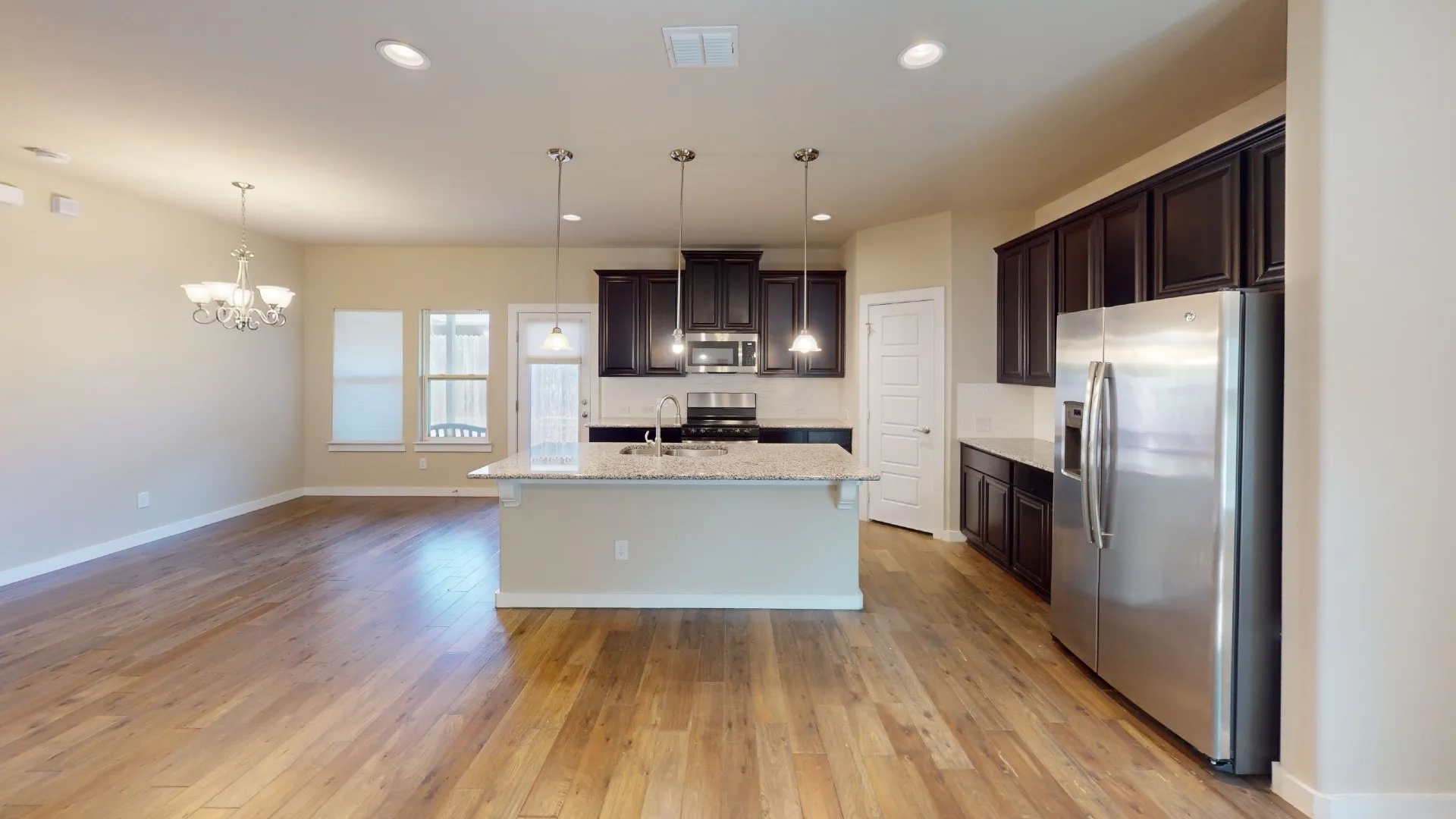 Wood-finish flooring throughout, kitchen island with built-in sink, dark wood cabinetry, stainless steel refrigerator, and recessed lighting