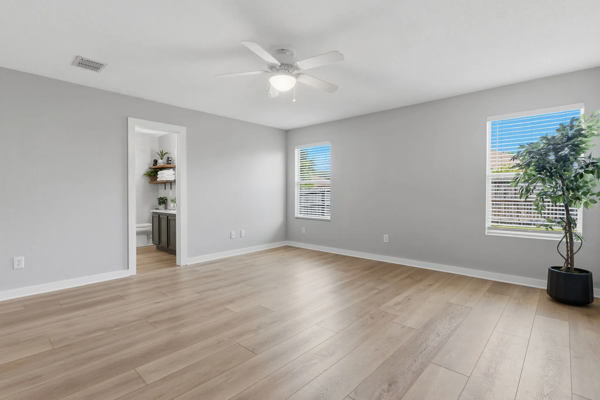 Spacious primary suite features LVP flooring, a ceiling fan, neutral finishes and multiple windows for natural light.