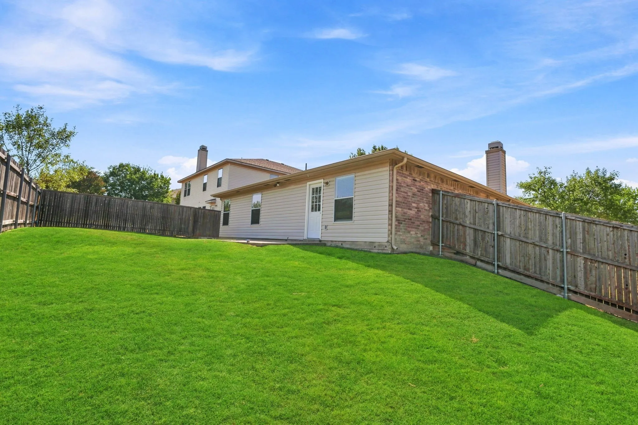 Rear exterior view showcases the single-story layout, fenced yard and open grassy space behind the home.