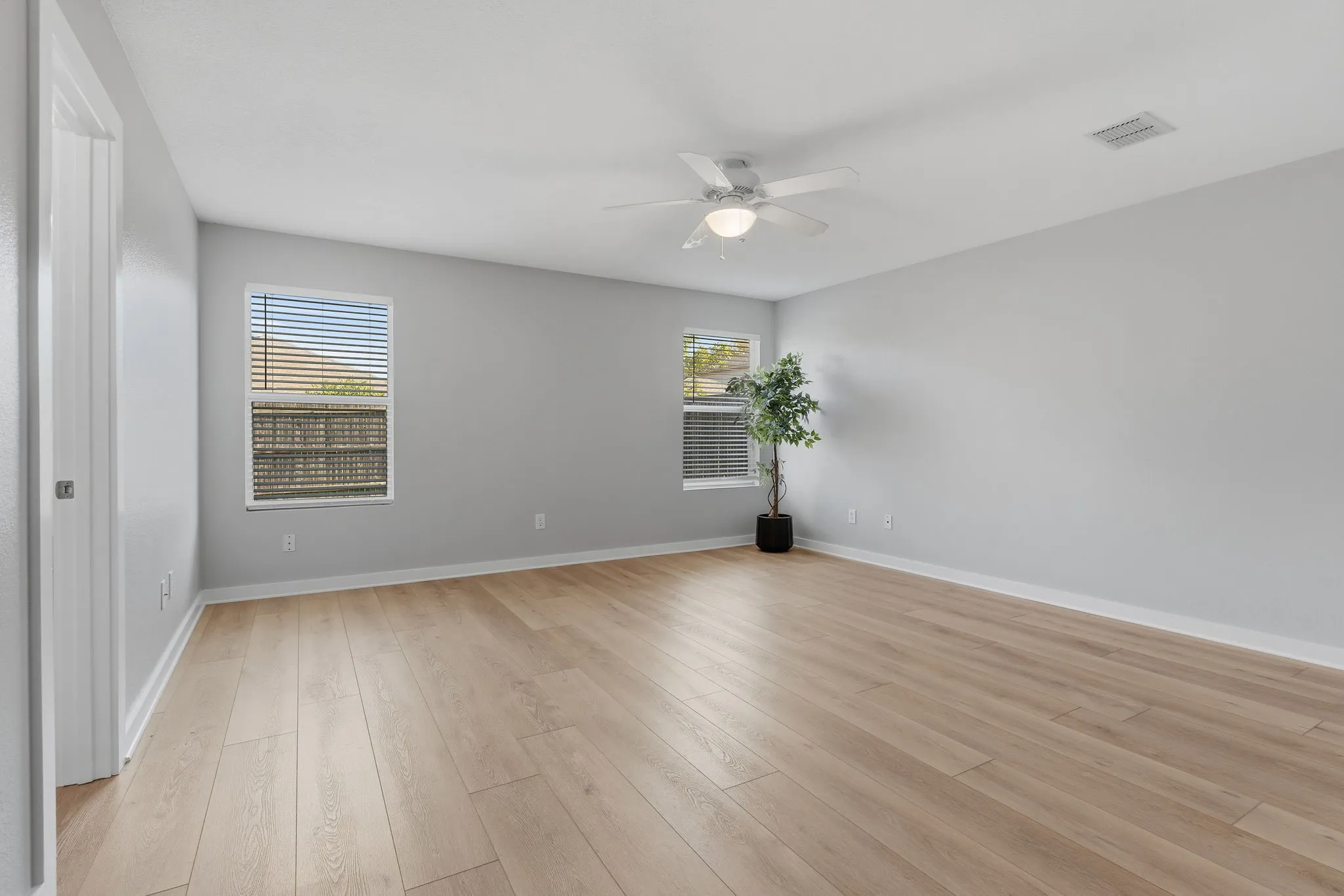 Spacious primary suite features LVP flooring, a ceiling fan, neutral finishes and multiple windows for natural light.