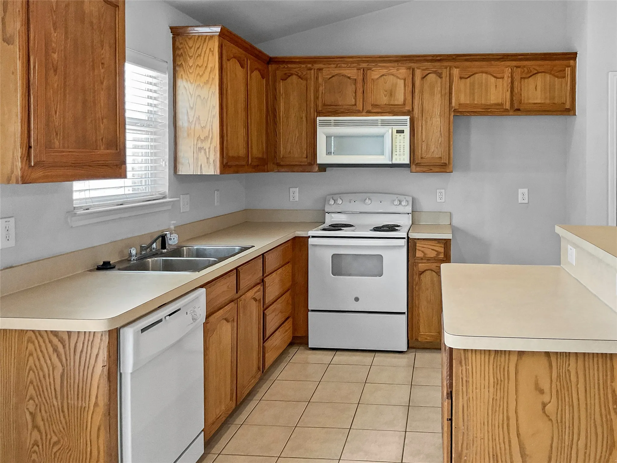 Kitchen featuring sink, vaulted ceiling, light tile flooring, and white appliances