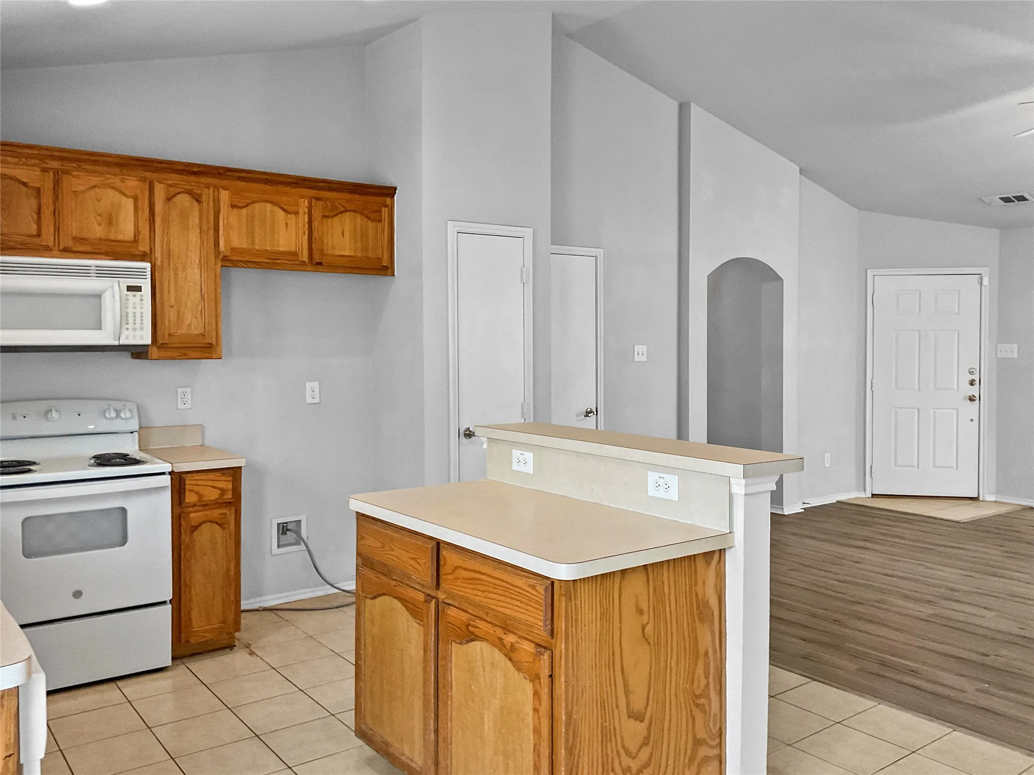 Kitchen with vaulted ceiling, a center island, white appliances, and light tile floors