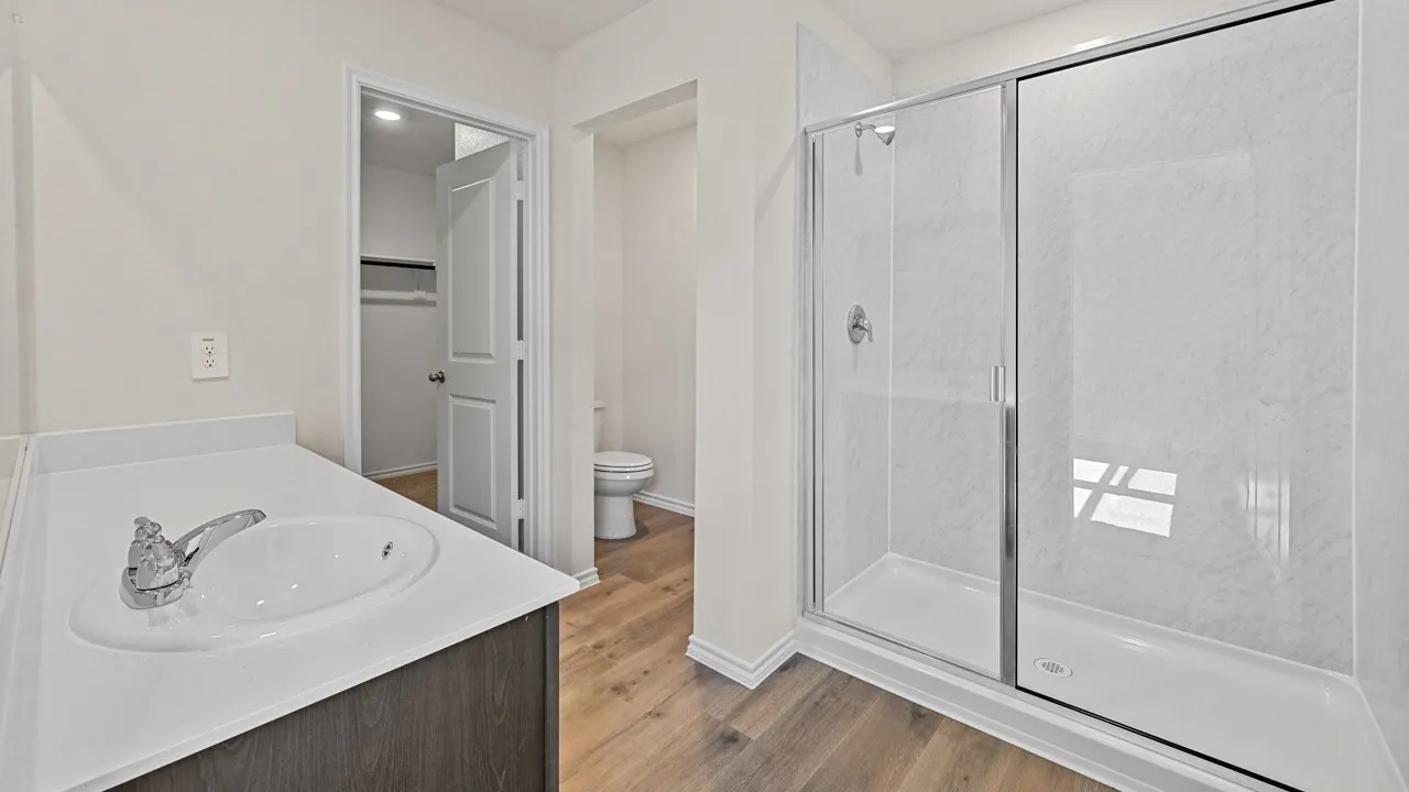 Walk-in shower with a glass enclosure, single vanity with an integrated sink, wood-finish flooring, and a built-in closet with shelving