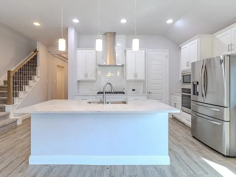 Open-concept kitchen featuring an expansive island with a built-in sink, white shaker cabinetry, stainless steel appliances, and wood-finish flooring