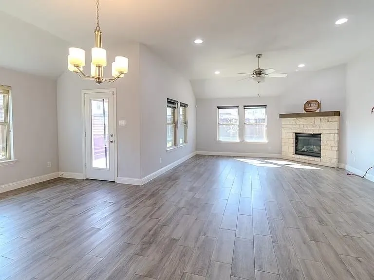 Spacious room featuring vaulted ceilings, recessed lighting, wood-finish flooring, a stone fireplace with a wood mantle, and multiple windows