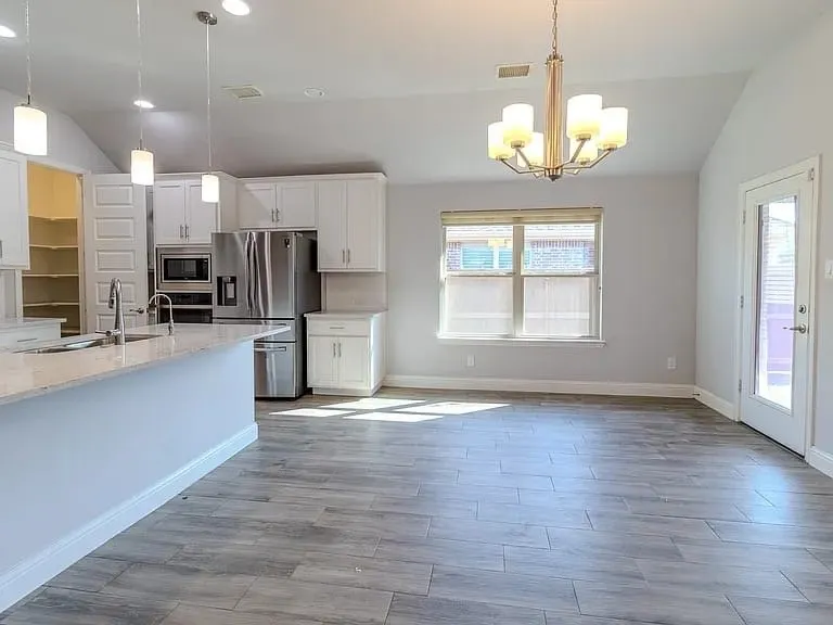 Kitchen featuring a large island with sink, white shaker cabinetry, stainless steel appliances, and wood-finish flooring