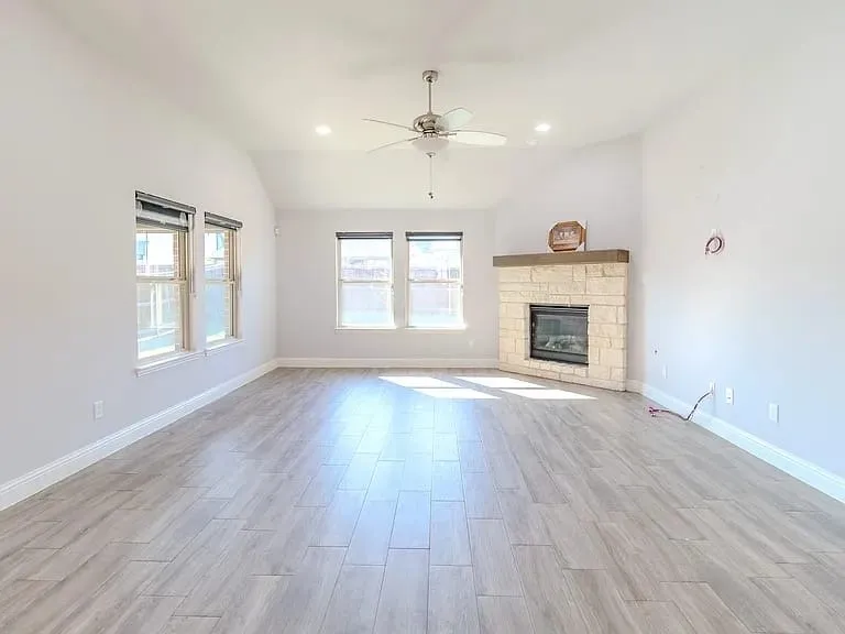 Vaulted ceiling with a ceiling fan, stone-clad fireplace with a wood mantle, recessed lighting, multiple windows, and tile flooring
