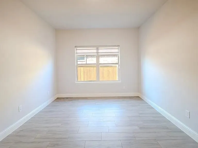 White walls with a window featuring blinds, wood-finish flooring, and white trim