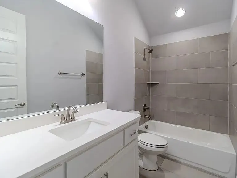 Contemporary bathroom featuring a white vanity with an integrated sink, brushed nickel faucet, large wall mirror, and a tiled tub/shower combination with a built-in shelf