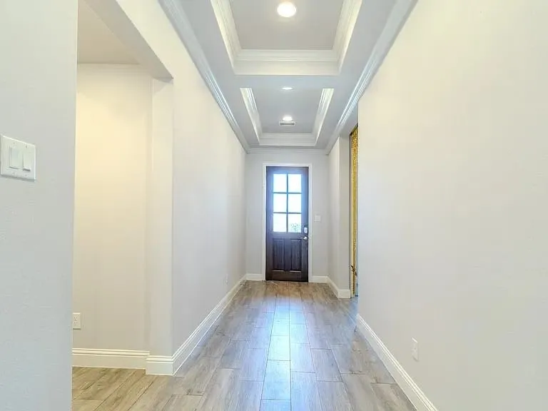 Recessed lighting illuminates the coffered ceiling, wood-finish flooring, and solid core door with glass panels