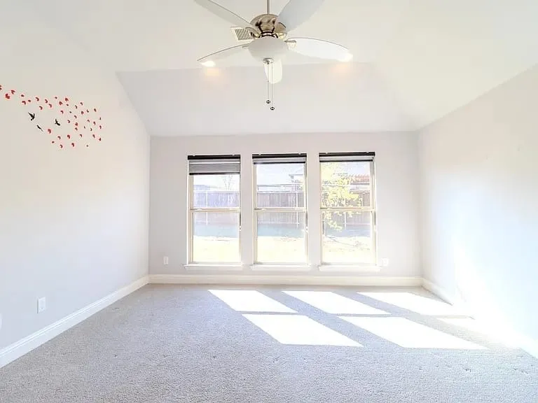 Vaulted ceiling with a flush-mount ceiling fan, three pane windows with roller shades, and carpet flooring
