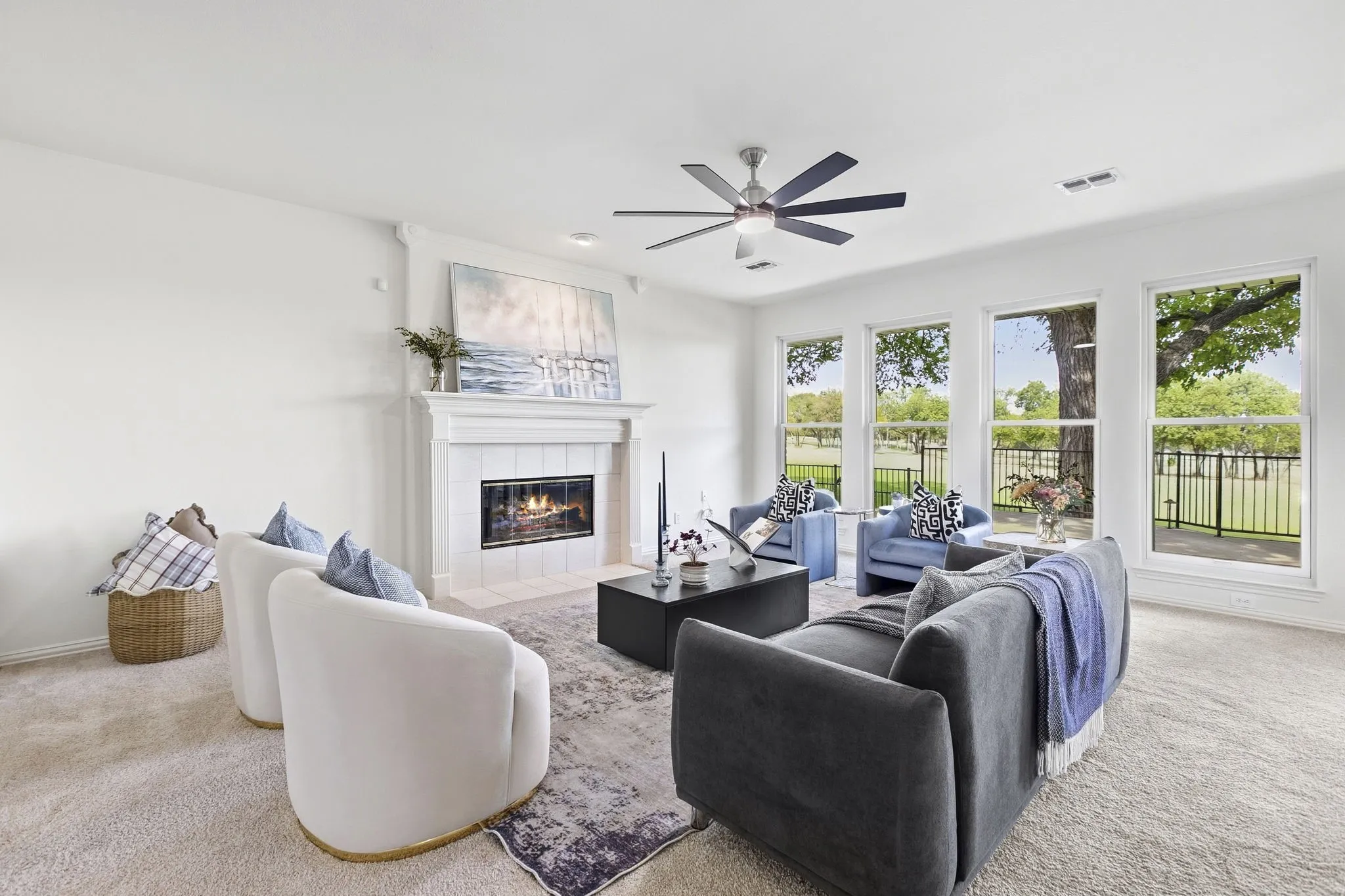 Spacious living area open to the kitchen, overlooking the golf course, featuring a fireplace with a white mantel, back wall lined with large windows, a new ceiling fan, and new carpet.